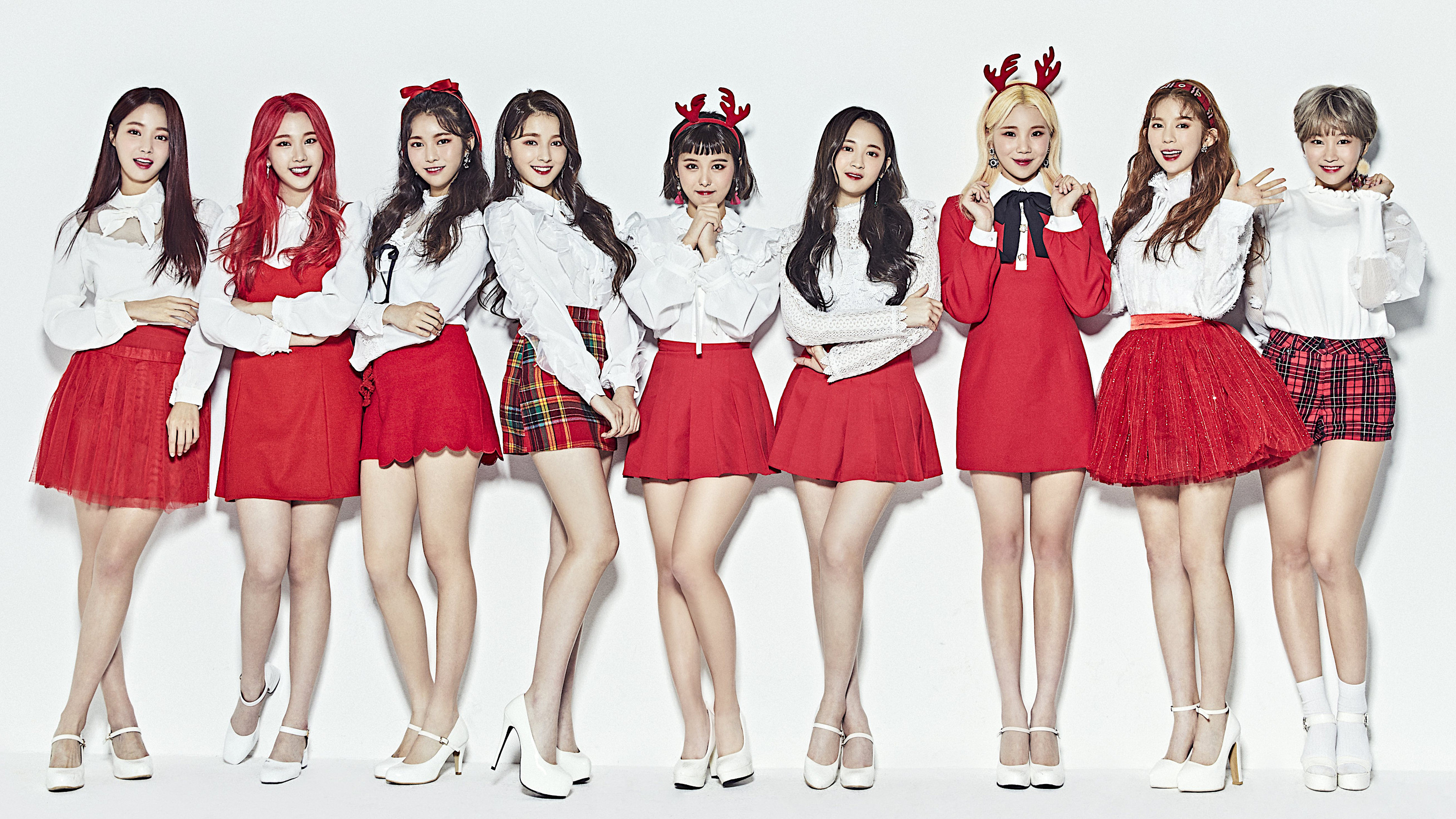 A picture of the beautiful Korean girl group Momoland: Hyebin, Yeonwoo, Jane, Taeha, Nayun, Daisy, JooE, Ahin and Nancy. They are wearing red and white sweaters and smiling at the camera.