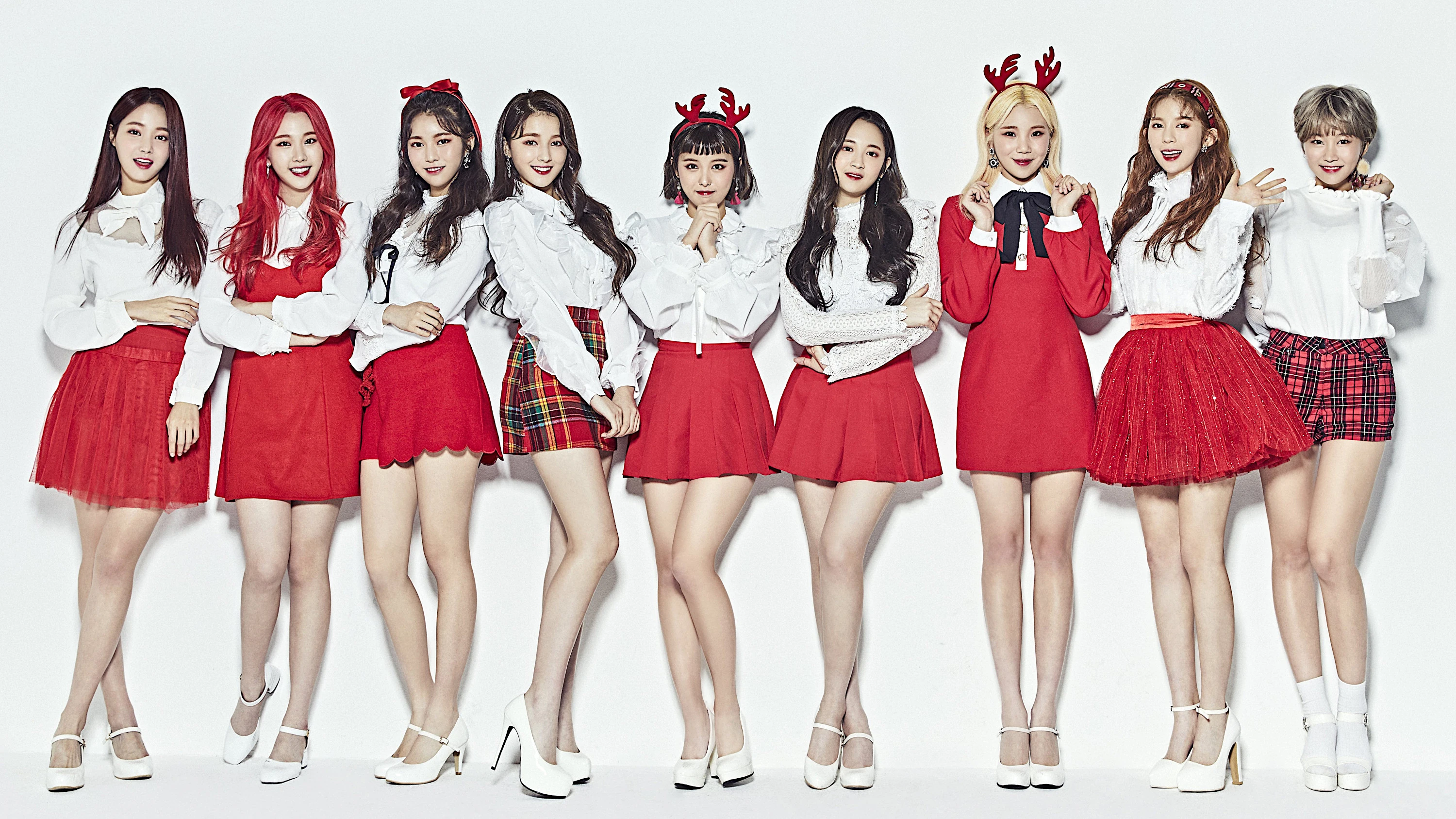 A picture of the beautiful Korean girl group Momoland: Hyebin, Yeonwoo, Jane, Taeha, Nayun, Daisy, JooE, Ahin and Nancy. They are wearing red and white sweaters and smiling at the camera.